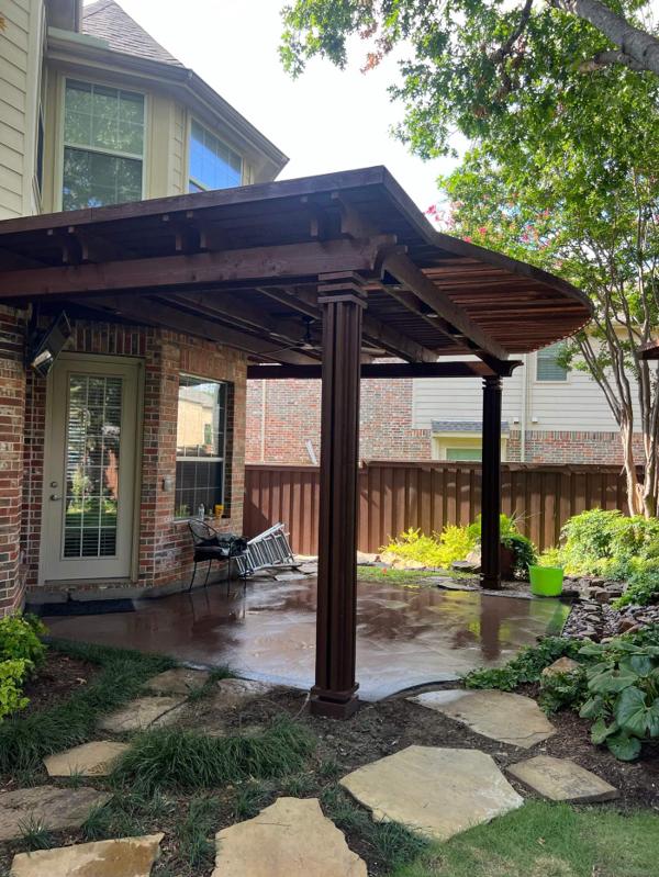 Attached stained wood patio cover along the back of a brick home