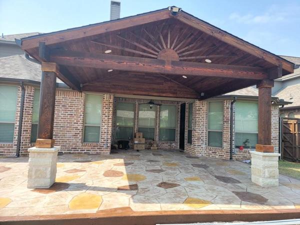 Stained wood gable patio cover with a sunburst gable detail, stone column bases and a flagstone patio