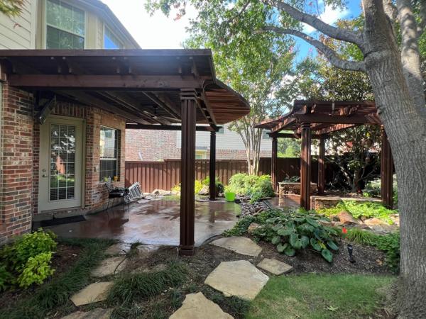 Two stained wood pergolas over a stained concrete patio with a flagstone walkway