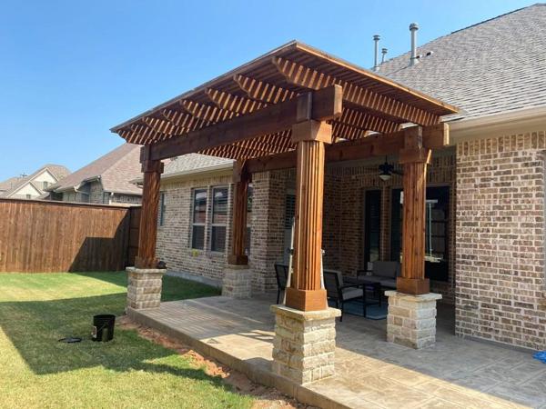 Attached stained wood pergola on stone column bases over a backyard patio